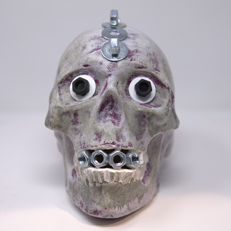 Gray painted skull with shading in purple and metal embellishments.