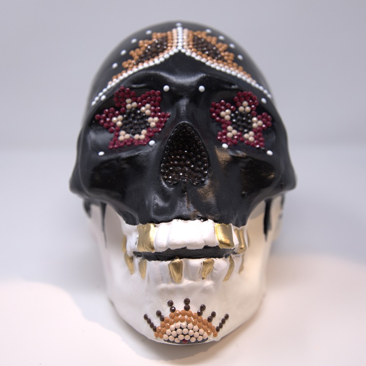 White skull with the top half painted black featuring beading designs in brown, beige, maroon, black and white.,