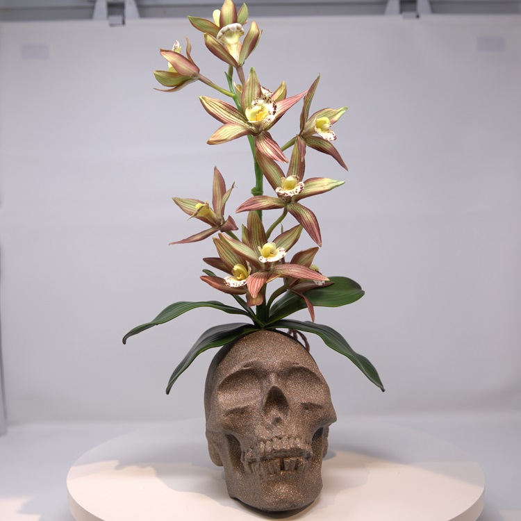 Skull decorated to mimic a cement plant pot with artificial flowers growing form it.