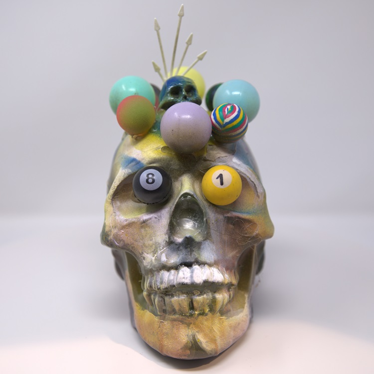 Artistically painted skull in yellow, gray, lavender and white, with a crown of globes and poll ball eyes. 