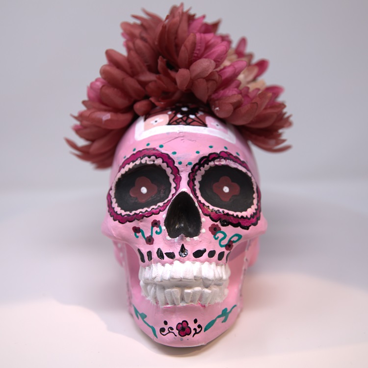 Pink painted skull with flower and dotted decorations in magenta, black, green and white, featuring a crown of flowers.