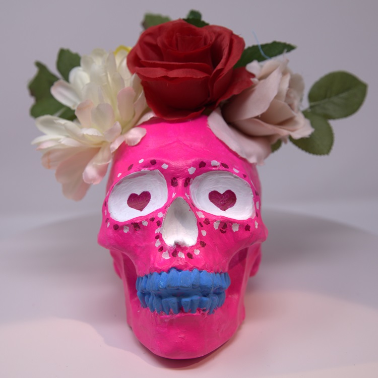 Pink painted skull inspired by Barbie with decorative flowers, and painted features in white, red and blue.