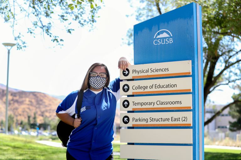 student leaning against directional sign 