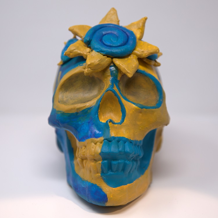 Blue and gold painted skull with a hand-sculpted sun on it's head.