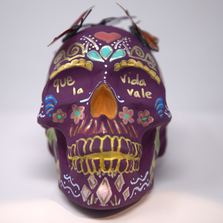 Purple painted skull with detailing in gold, turquoise, blue, pink and orange, featuring butterflies on its head.