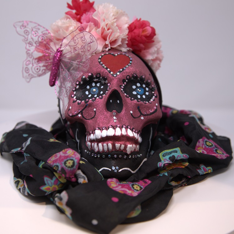 Pink painted skull with a red heart and details in black, a crown of flowers and a butterfly in commemoration of Breast Cancer Awareness Month