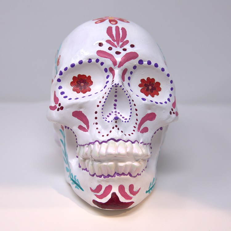 White skull with decorative flower, dot, and line patterns in red, pink, purple and turquoise. 