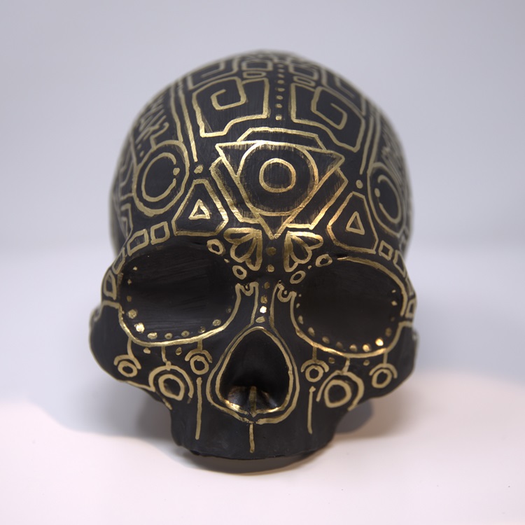 Half a skull painted in matte black with linear details in gold.