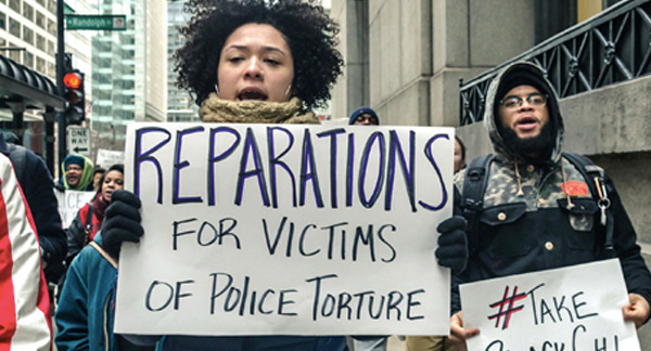 A protestor holds a sign reading "Reparations for victims of police torture."